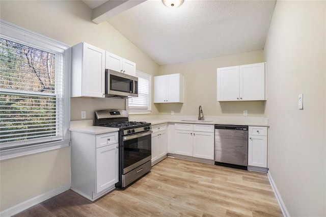 kitchen featuring vaulted ceiling with beams, sink, white cabinets, stainless steel appliances, and light hardwood / wood-style flooring