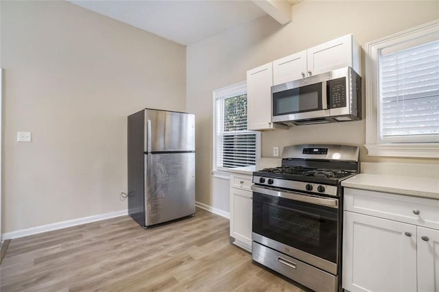 kitchen featuring white cabinetry, light hardwood / wood-style flooring, stainless steel appliances, and beamed ceiling