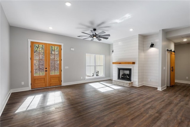 unfurnished living room featuring a barn door, ceiling fan, dark hardwood / wood-style flooring, and a brick fireplace