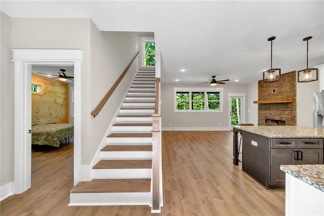 staircase featuring ceiling fan, wood-type flooring, and a stone fireplace