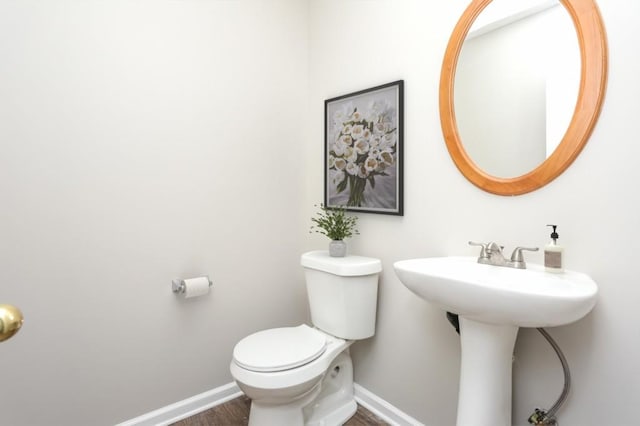 bathroom featuring baseboards, toilet, wood finished floors, and a sink