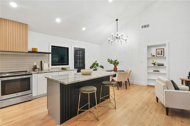 kitchen featuring a breakfast bar, hanging light fixtures, stainless steel stove, light hardwood / wood-style flooring, and white cabinetry