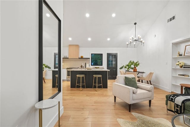 living room with built in features, light wood-type flooring, high vaulted ceiling, and an inviting chandelier