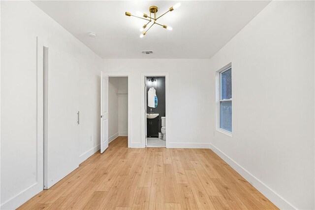 unfurnished bedroom with an inviting chandelier, ensuite bathroom, sink, light hardwood / wood-style floors, and a closet