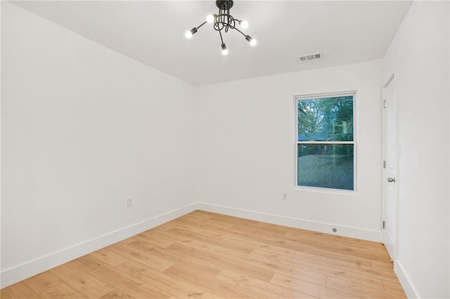 spare room featuring light wood-type flooring and a notable chandelier