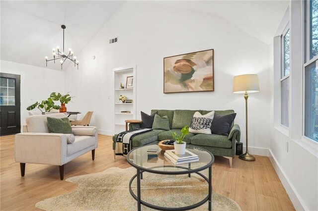 living room featuring built in shelves, high vaulted ceiling, light hardwood / wood-style floors, and a notable chandelier