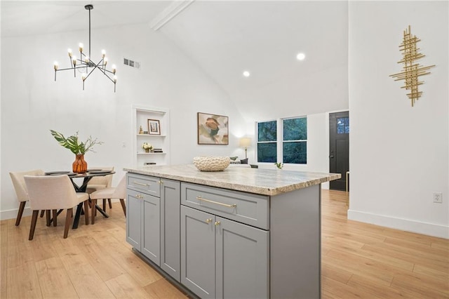 kitchen featuring beam ceiling, light hardwood / wood-style flooring, decorative light fixtures, gray cabinets, and a kitchen island