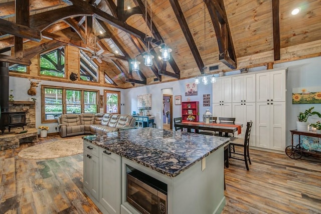 kitchen featuring high vaulted ceiling, beam ceiling, a wood stove, and white cabinetry