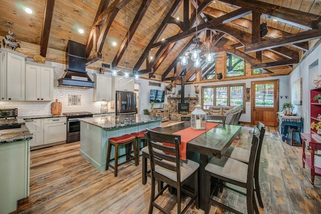 dining room with beam ceiling, a wood stove, wooden ceiling, and light wood-type flooring