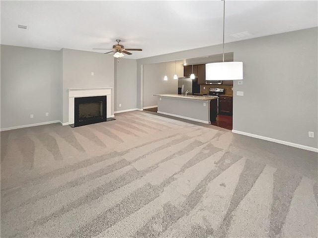 unfurnished living room featuring ceiling fan, sink, and carpet floors