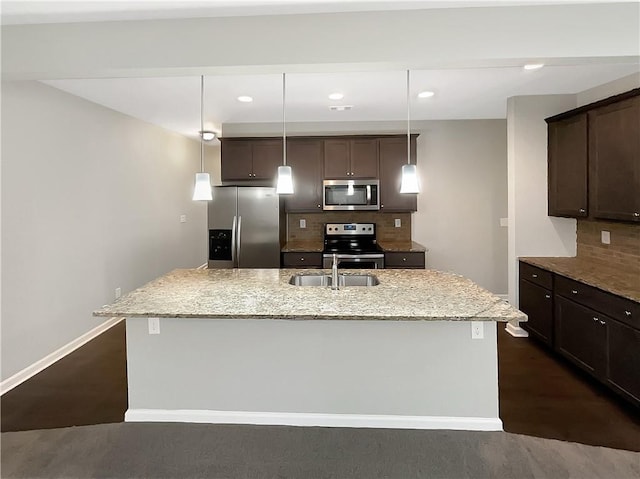 kitchen featuring light stone countertops, tasteful backsplash, stainless steel appliances, a center island with sink, and hanging light fixtures