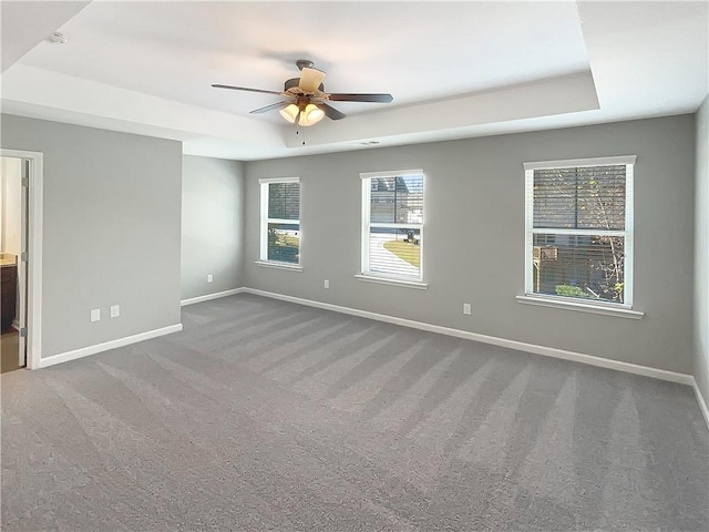 carpeted empty room with a raised ceiling and ceiling fan