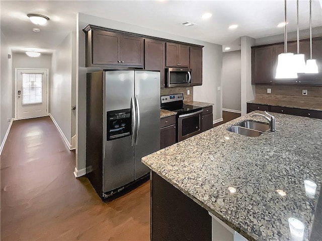 kitchen with pendant lighting, sink, appliances with stainless steel finishes, light stone counters, and dark brown cabinetry