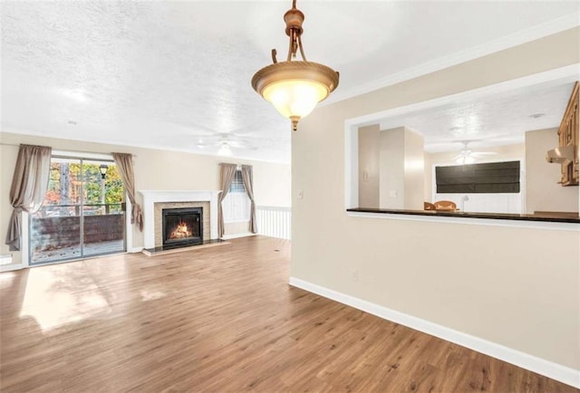 unfurnished living room with ceiling fan, a warm lit fireplace, wood finished floors, baseboards, and a textured ceiling