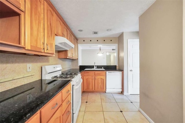 kitchen featuring white appliances, under cabinet range hood, a sink, light tile patterned flooring, and dark stone countertops