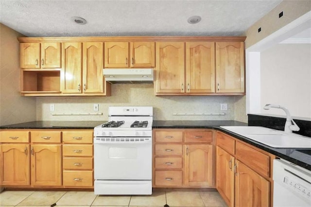 kitchen featuring white appliances, under cabinet range hood, a sink, dark countertops, and light tile patterned flooring