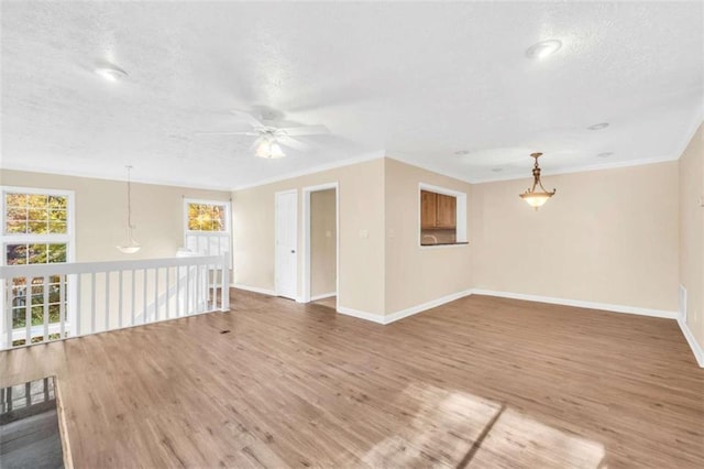 unfurnished living room with ceiling fan, wood finished floors, baseboards, crown molding, and a textured ceiling