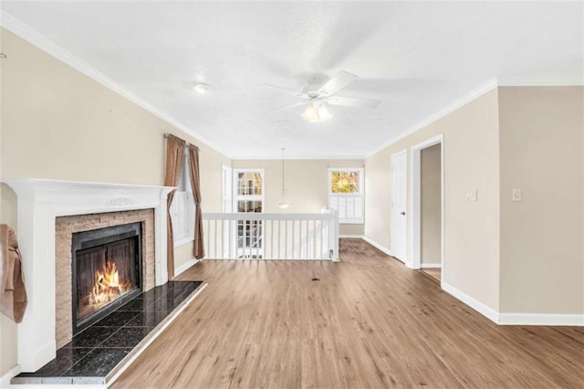unfurnished living room with a ceiling fan, baseboards, wood finished floors, a tile fireplace, and crown molding
