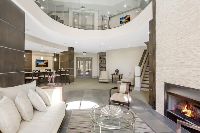 carpeted living area with a high ceiling, a fireplace, recessed lighting, stairs, and french doors