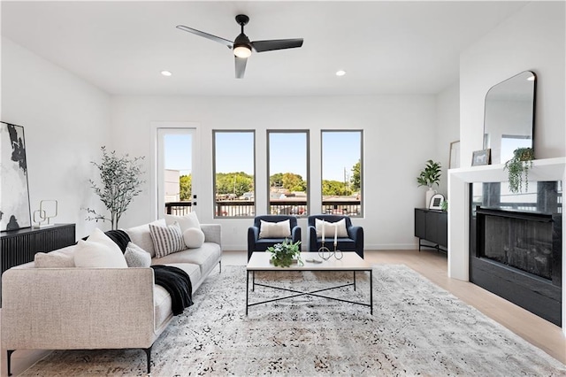 living room with a premium fireplace, a wealth of natural light, ceiling fan, and light hardwood / wood-style flooring