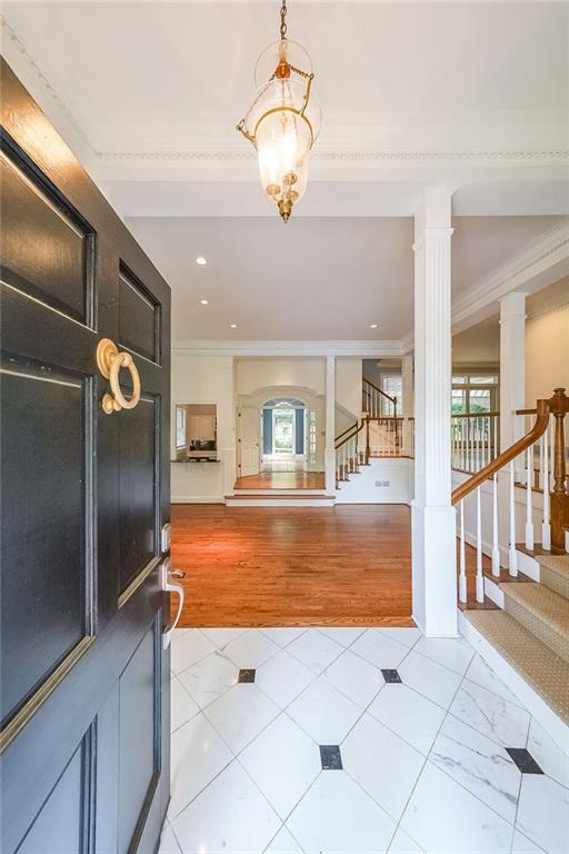 entryway featuring light hardwood / wood-style flooring, a notable chandelier, ornamental molding, and ornate columns