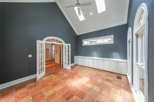 tiled empty room with a skylight, ceiling fan, french doors, high vaulted ceiling, and crown molding