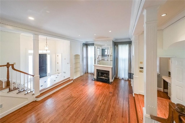 unfurnished living room with ornate columns, crown molding, a fireplace, and wood-type flooring