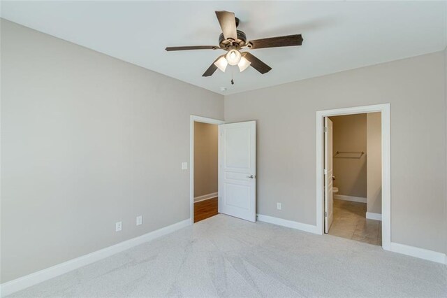 unfurnished bedroom with ceiling fan, light colored carpet, a closet, and a walk in closet