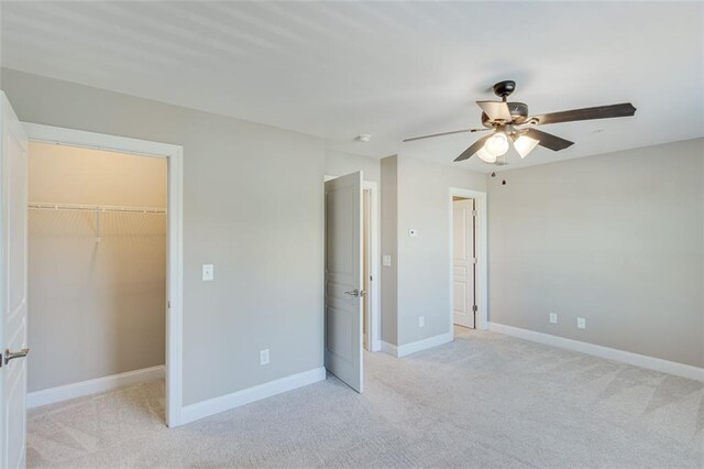 unfurnished bedroom with light carpet, ceiling fan, a walk in closet, and a closet