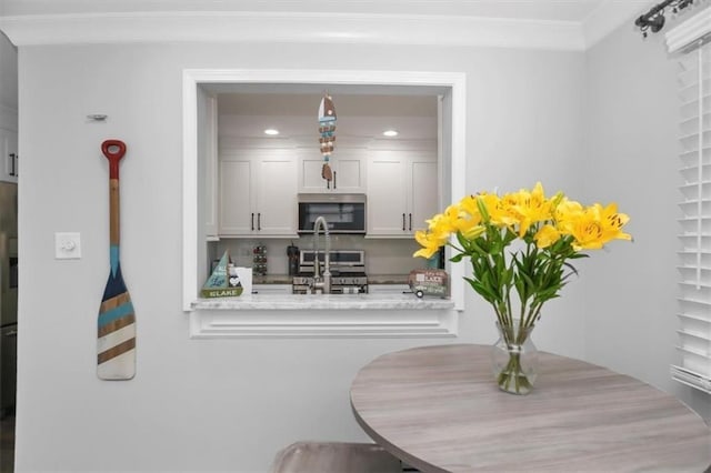 kitchen featuring light stone countertops, white cabinets, appliances with stainless steel finishes, and ornamental molding