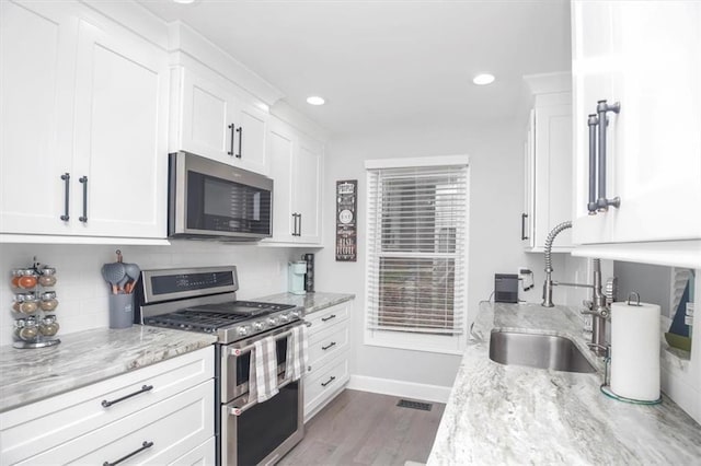 kitchen featuring appliances with stainless steel finishes, white cabinetry, light hardwood / wood-style floors, sink, and light stone counters