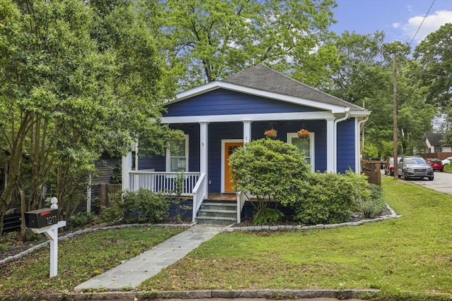 view of front facade with covered porch, a front yard, and a shingled roof