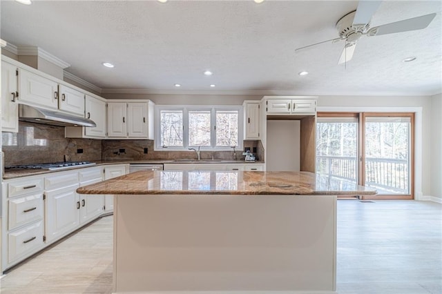 kitchen featuring white cabinetry, light stone counters, a wealth of natural light, a kitchen island, and stainless steel gas stovetop