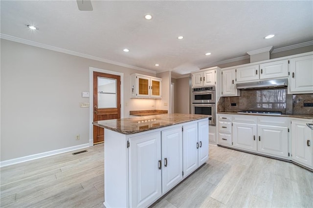 kitchen with a kitchen island, white cabinetry, dark stone counters, gas cooktop, and stainless steel double oven