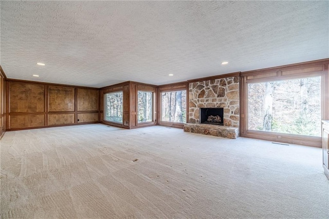 unfurnished living room with a stone fireplace, wooden walls, light colored carpet, and a textured ceiling