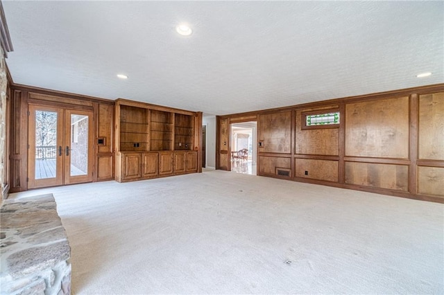 unfurnished living room featuring french doors, light carpet, and wood walls