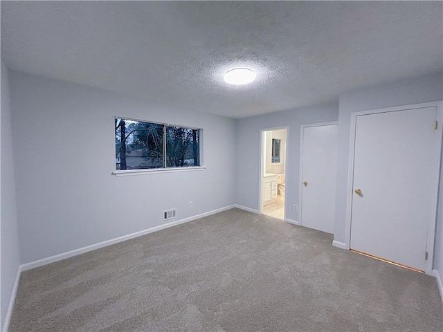 unfurnished bedroom featuring ensuite bathroom, light colored carpet, and a textured ceiling