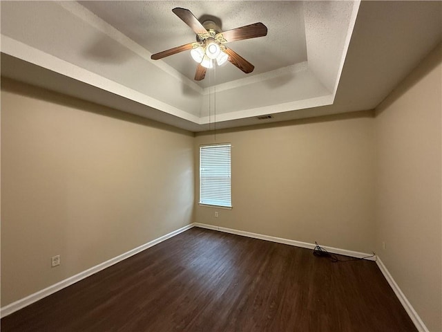 empty room featuring visible vents, dark wood-type flooring, ceiling fan, baseboards, and a raised ceiling