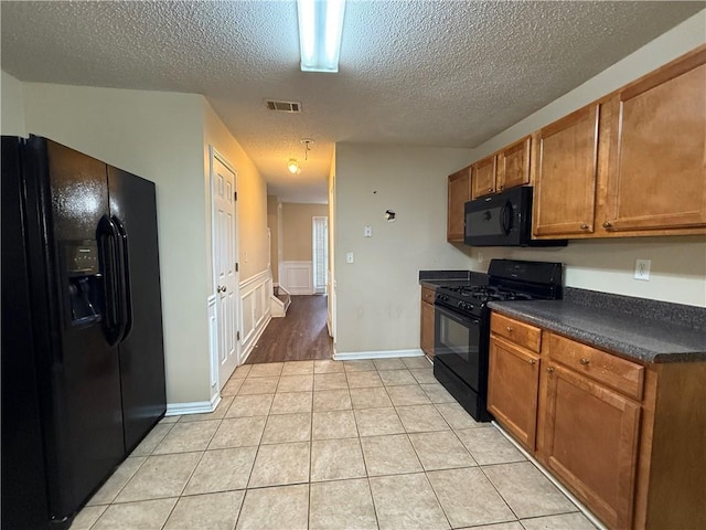 kitchen with light tile patterned floors, brown cabinetry, visible vents, black appliances, and dark countertops