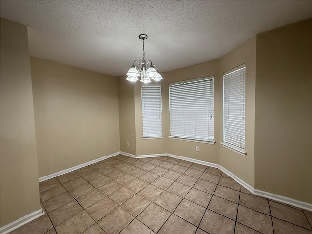 spare room featuring baseboards, a notable chandelier, light tile patterned flooring, and a textured ceiling