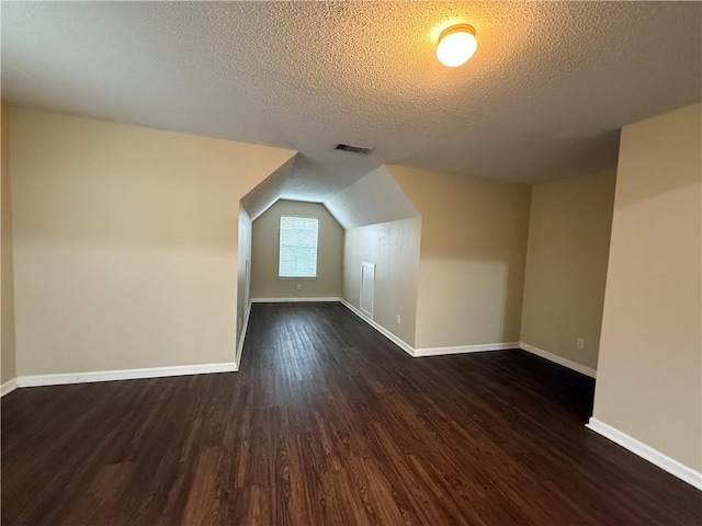 additional living space with visible vents, baseboards, a textured ceiling, and dark wood-style flooring