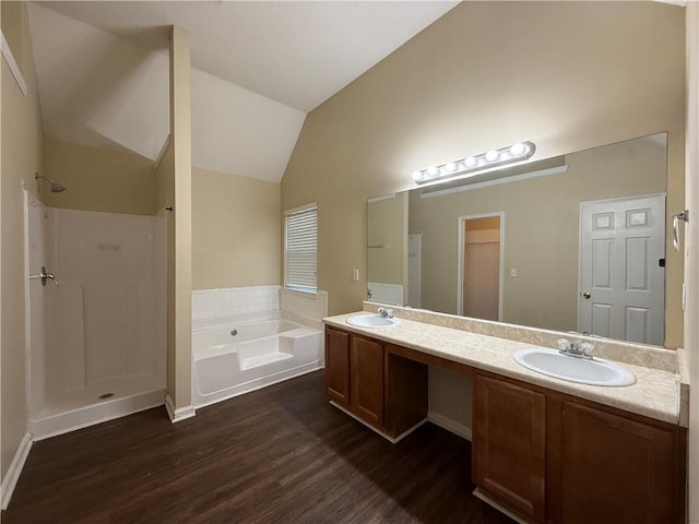 bathroom with wood finished floors, lofted ceiling, double vanity, a sink, and a bath