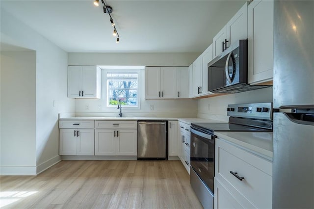 kitchen with white cabinets, appliances with stainless steel finishes, a sink, and light wood finished floors