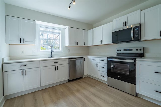 kitchen with appliances with stainless steel finishes, a sink, light wood-style floors, light countertops, and white cabinetry