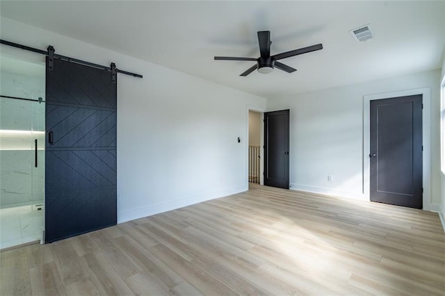unfurnished bedroom featuring ceiling fan, visible vents, a barn door, and light wood-type flooring