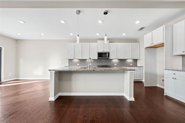 kitchen with white cabinetry, pendant lighting, an island with sink, and light stone counters