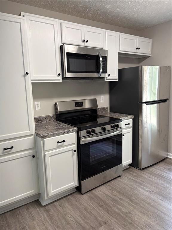 6103 Chaseland Dr, Rex, GA 30273 - kitchen featuring appliances with stainless steel finishes, light wood-type flooring, white cabinetry, a textured ceiling, and dark stone countertops