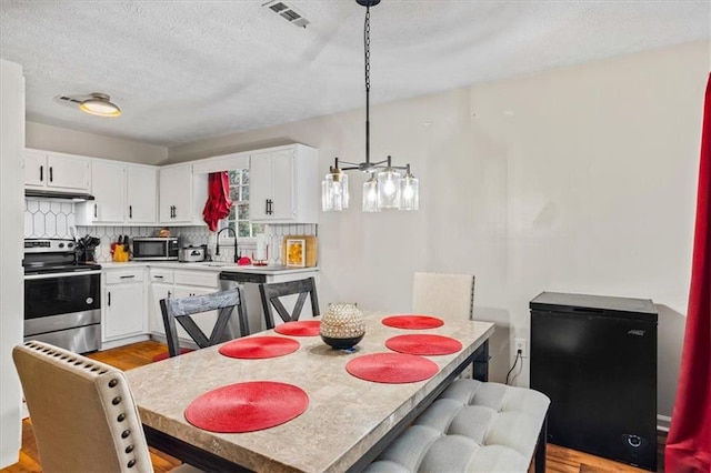 dining room with sink, a textured ceiling, and light hardwood / wood-style flooring