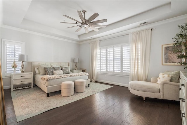 bedroom featuring dark wood-style floors, a tray ceiling, visible vents, and baseboards