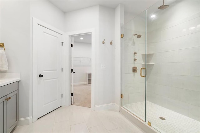 bathroom with a walk in closet, a stall shower, vanity, tile patterned flooring, and baseboards